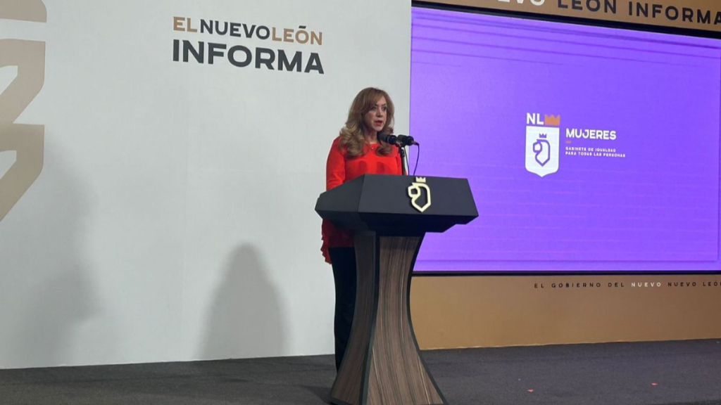 Woman in a Red Blouse Speaks at a Dark Lectern on a Stage, with 'el Nuevo LeÓn Informa' Backdrop Behind Her. - Glen Facturero