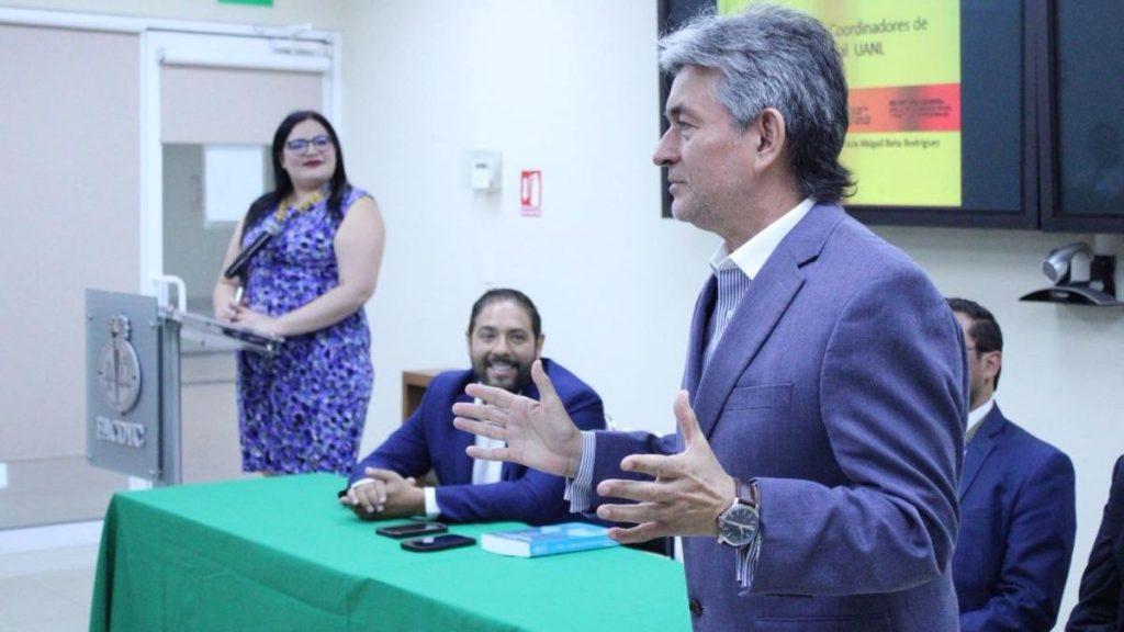 Man in a Blue Suit Speaks at a Panel with Others Seated at a Green-clothed Table in a Conference Room. - Glen Facturero