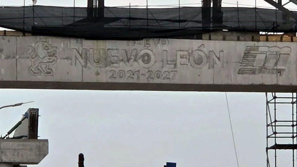Construction Site with a Graffiti-covered Concrete Beam Reading 'nuevo LeÓn 2021-2027' and Logos Against a Gray Sky - Glen Facturero