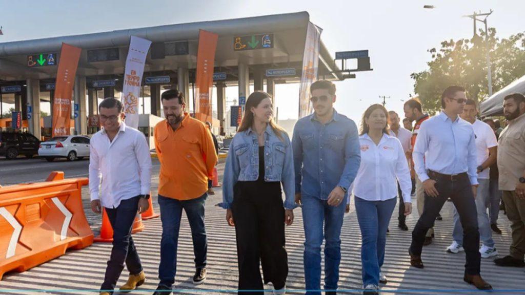 Group of People Walking Across a Toll Plaza, with Orange Barriers and Banners Behind Them, During Daylight. - Glen Facturero