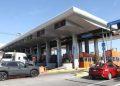 Airport Toll Plaza with Multiple Lanes Under a Curved White Roof, Orange Service Kiosks, and Passing Cars. - Glen Facturero