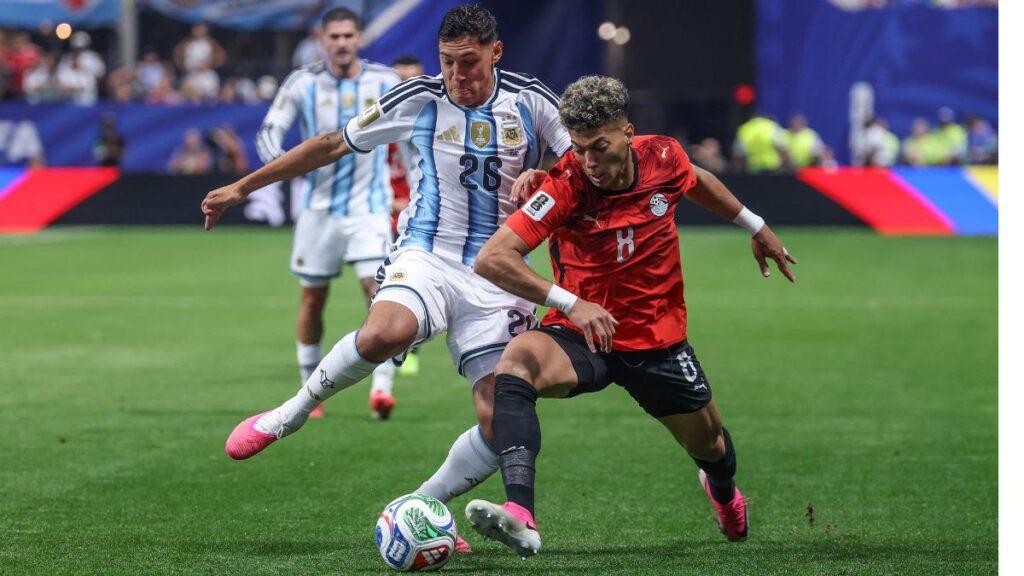 Bloque 2- Junio 46 - Glen Facturero Two Soccer Players, One in a Blue-and-white Striped Jersey and One in Red, Contest the Ball on a Green Pitch During a Match Iron-tight Duel. - Glen Facturero