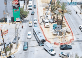 Aerial view of a busy street under construction with a circular median containing a palm tree and construction equipment, and cars around it.
