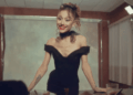 Woman in an Off-shoulder Black Dress with Red Lipstick and Sunglasses on Her Head, Smiling Behind a Table in a Photography Studio. - Glen Facturero