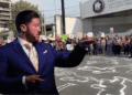 a Man in a Blue Suit Gestures Toward a Crowd of Protesters Holding Signs, with Chalk Outlines on the Pavement Behind Them Near a Justice Building. - Glen Facturero