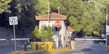Small Security Booth at a Gated Entrance with a Red 'alto' Stop Sign, Barrier Gate, and Yellow Planters Nearby. - Glen Facturero
